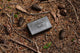 Pine tar soap bar sits on a forest floor next to pinecones.